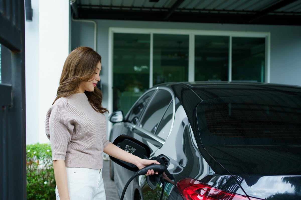 Woman charges her electric vehicle at home, illustrating the convenience of modern transportation and eco-friendly living. Clean energy usage, sustainability, and the growing adoption of electric car.